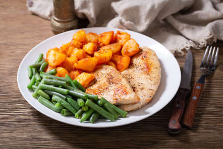 Plate of grilled turkey chops, baked potatoes and green beans on wooden tableの写真素材