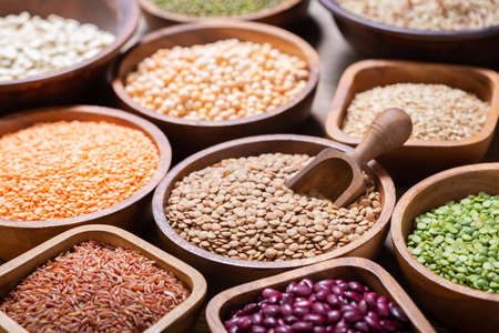 bowls of legumes, lentils, chickpeas, beans, rice and cereals on a wooden backgroundの写真素材