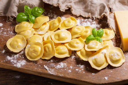Fresh ravioli with green basil on wooden board, top viewの写真素材