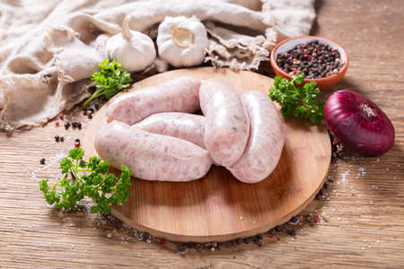 Fresh sausages with spices and vegetables on a wooden boardの写真素材