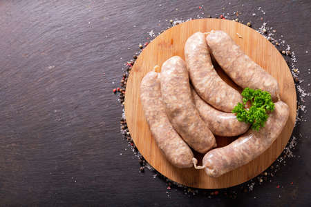 Fresh sausages on a chopping board on dark background, top viewの写真素材