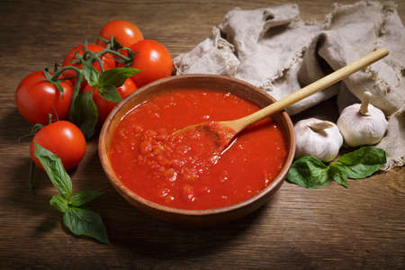 bowl of tomato sauce and fresh vegetables on a wooden tableの写真素材
