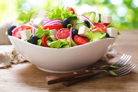 Bowl of fresh salad with vegetables on a wooden tableの写真素材