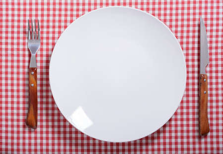 empty plate with fork and knife on red tablecloth, top viewの写真素材