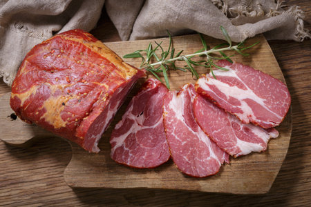Slices of smoked ham with rosemary on wooden board, top viewの写真素材