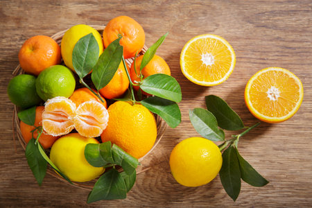 Plate of fresh citrus fruits with leaves on a wooden table, top viewの写真素材