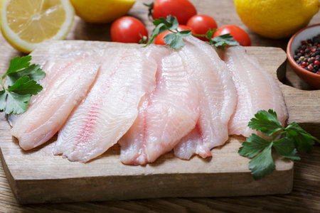 fresh fish fillet of tilapia with ingredients for cooking on wooden boardの写真素材