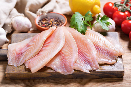 fresh fish fillet of tilapia with ingredients for cooking on wooden boardの写真素材