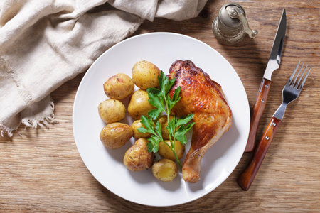 plate of baked chicken leg with potatoes on wooden background, top viewの写真素材