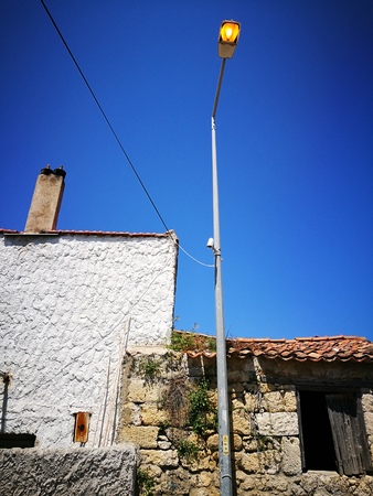 Street light burning in the daylight in front of sunny blue skyの写真素材