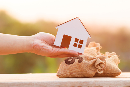 Buying a new house, saving and finance loan concept. Hand put house on money bags with Dollar sign on woodle desk at sunset and green nature backgroundの写真素材