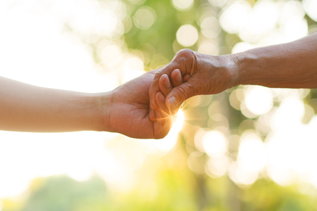 Hand of young man holds Elder person hand with love. metaphor Support, help, nursing home or help for elderly concept.の写真素材