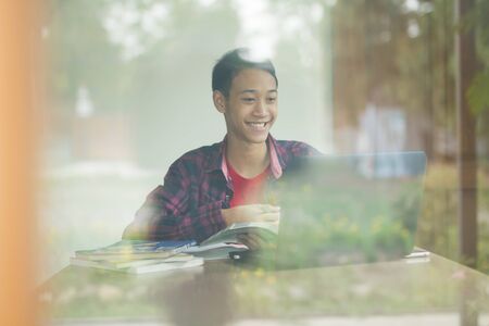 Happy young asia man smiling and feeling fun while studying online with tutor on laptop at home. global education, online study and e-learning concept.の写真素材