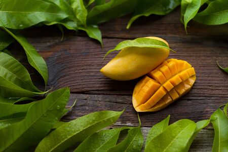 Mango fruit with green tropical leaf on wooden backgroundの写真素材