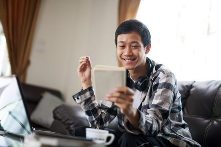 Happy asian man enjoying his online class at home, teaching by a tutor or teacher through laptop...
