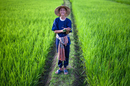 Young asian farmer with hat and tradition costume laughing at green rice fields metaphor hapiness...