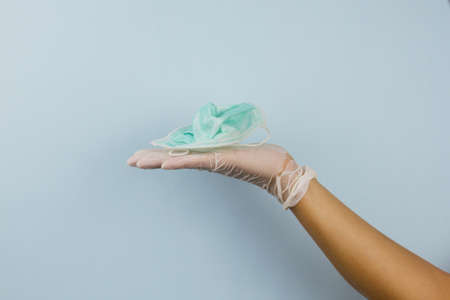 used surgical mask, face mask put on a hand of a doctor with blue background. wash surgical mask or trash it for prevention of spread of corona virus, Covid-19の写真素材