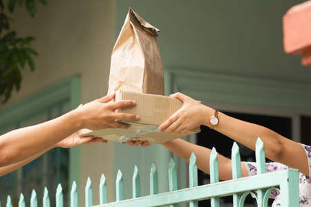 Hand of woman taking a package and food box from delivery man at homeの写真素材