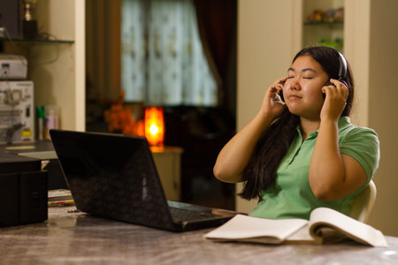 Asian girl listening music while using laptop computer at home. Night scene. online class and...