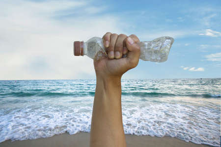 Hand hold plastic bottle tightly with ocean on background. Protect an environment from plastic pollution concept.の写真素材