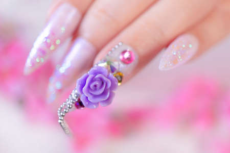 close up woman hand manicure with long acrylic extension stiletto style painting sweet ombre pink glitter decorated with beautiful light purple rose and sparkling rhinesotne for valentimeの写真素材