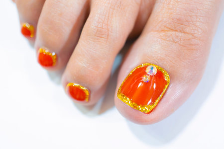 Close up Beautiful bright orange color gel polish painting on woman toenail decorated with sparkling...