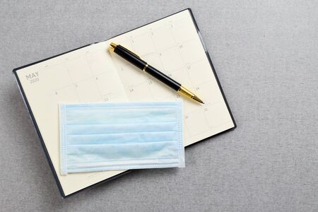 Black and gold fountain pen placed on blank planner book with medical protective mask on gray cement texture background. Work and health concept.の写真素材