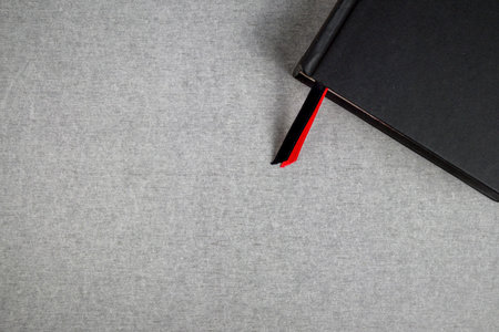 Black cover book with red and black bookmark on gray cement texture background and space.