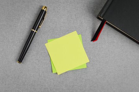 Blank yellow sticky note with black and gold fountain pen and black cover book with red and black bookmark on gray cement texture background.の写真素材