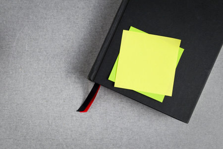 Blank yellow sticky note placed on black cover book with red and black bookmark on gray cement...