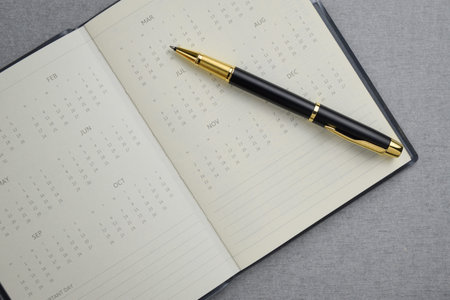 Black and gold fountain pen placed on calendar notebook on gray cement texture background. Task...