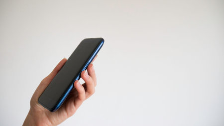 The left female hand holds a black mobile phone on a white background