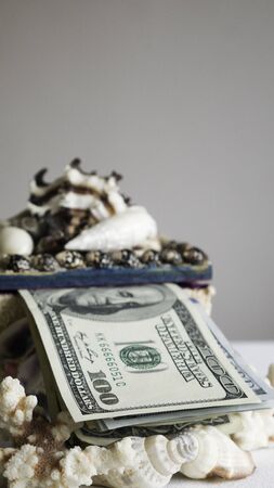 Stack of one hundred dollar bills in a box of seashellsの写真素材