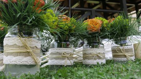 Bouquets of orange roses in glass retro vases on a green grassの写真素材