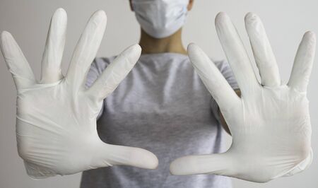 Woman with a medical mask and white latex glove shows the symbol STOP with both hands.の写真素材