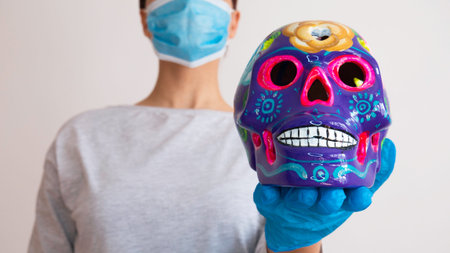 A woman with a surgical mask holding decorated colorful skulls. Day of dead, Mexico.