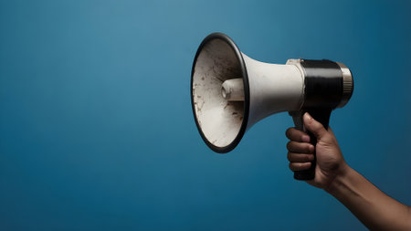 Hand holding a megaphone on a blue background with copy spaceの素材