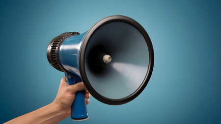 Male hand holding megaphone on blue background with copyspaceの素材