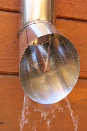 Water flow from the drainpipe, installed on the wooden wall.の写真素材