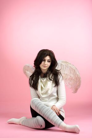 Sad angel sitting on the floor against pink backgroundの写真素材