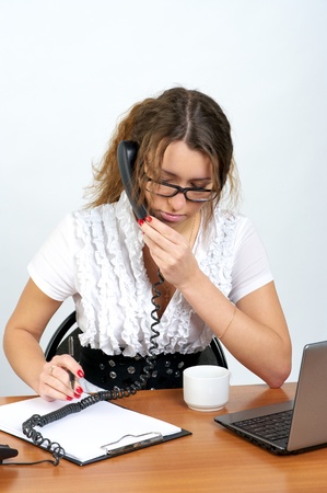 Cute business woman talking phone and writing something in the officeの写真素材
