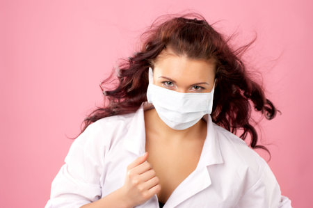 Portrait of young female doctor in mask against pink backgroundの写真素材