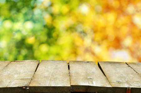 Bokeh of trees with green and orange colored leaves with wooden planks in the foregroundの写真素材