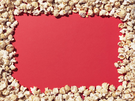 Shot of popcorn arranged to give a border to a plain, red area ideal for designer to add copy.の写真素材