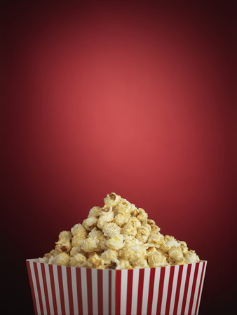 Shot of cinema style popcorn in a traditional striped box on a red backgroundの写真素材