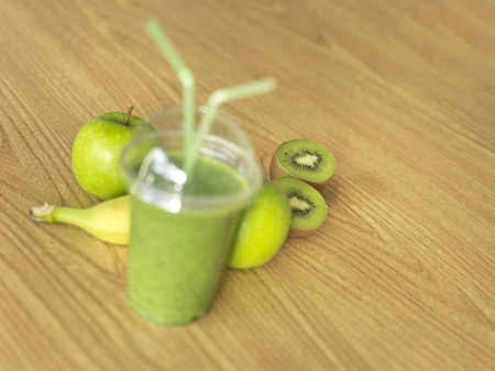 Shot of a green, take away, smoothie on a wooden table with selective focus on fruit in background.の写真素材