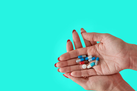 Colored assorted pharmaceutical medicine pills, tablets and capsules on female hand isoleted on light blue background. Close-up.の写真素材