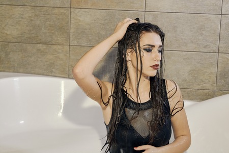 Young woman portrait with dripping smeared makeup dressed in the black bathing suit posing in the bathroom. Conceptual fashion photography for design. Young woman for lifestyle design.の写真素材