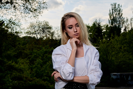 Young blonde woman in white skirt and shirt in the old sunny summer city park. Fashion woman. Young woman's modern portrait.の写真素材