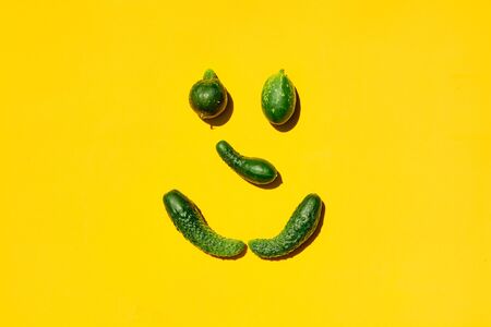 Different sizes and forms cucumbers on a yellow background forms a smiling face. Smile, face, emoji, smiley, happy smiley, happy emoji, smiling emoji. Top view. Concept for designers with copy space.の写真素材
